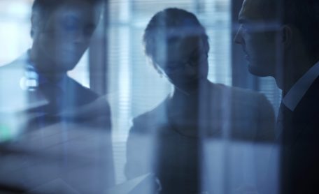 Blurred and darkened image of three office workers viewed through glass